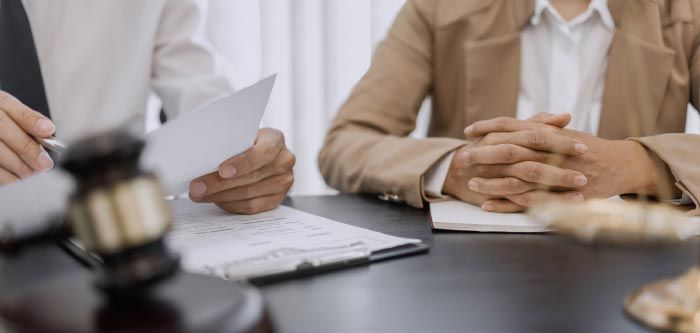 Two people at a desk, reviewing documents. Gavel and scales of justice in the foreground.
