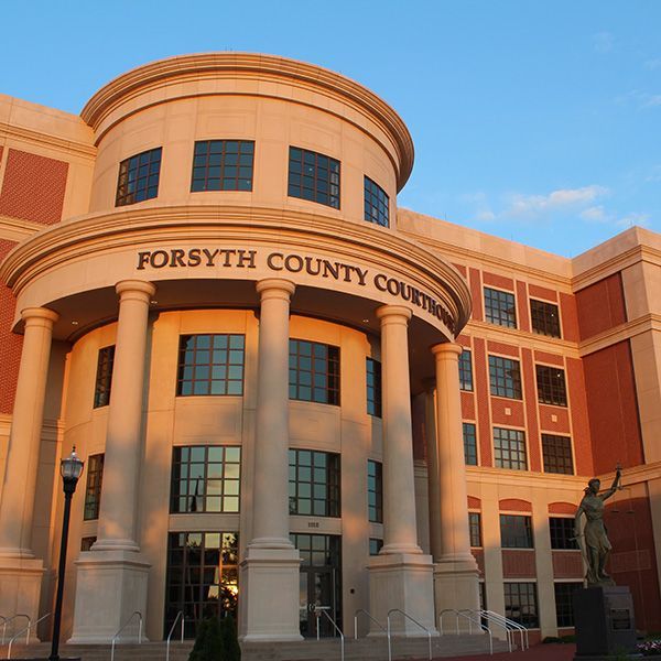 Forsyth County Courthouse building with columns, sign, and statue at sunset.