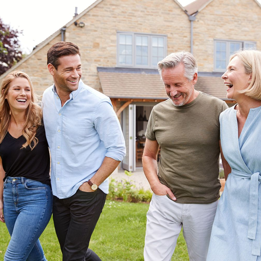 Four people smiling and walking on a lawn in front of a house.