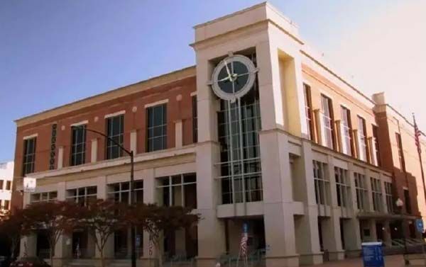 Brick building with a clock tower and multiple windows. The building is in front of a blue sky.