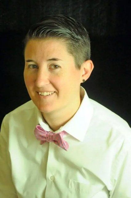 Person with short hair wearing a white shirt and pink bow tie, smiling.