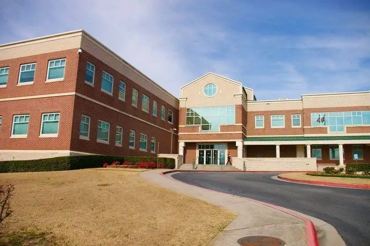 Brick building with multiple windows under a blue sky, accessed by a curving road.