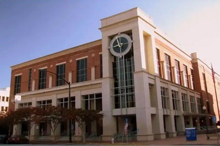 Brick and beige multi-story building with large clock tower; blue sky, sunny.