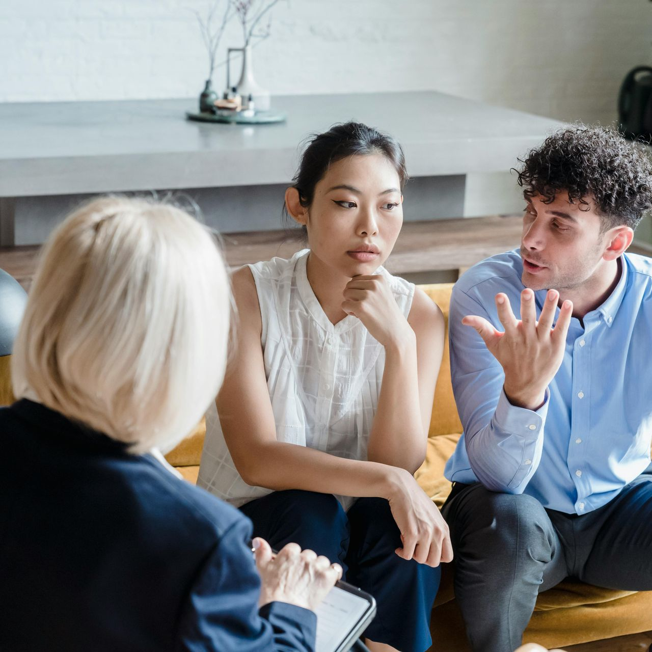 Couple talking with a therapist on a sofa. The therapist is taking notes.