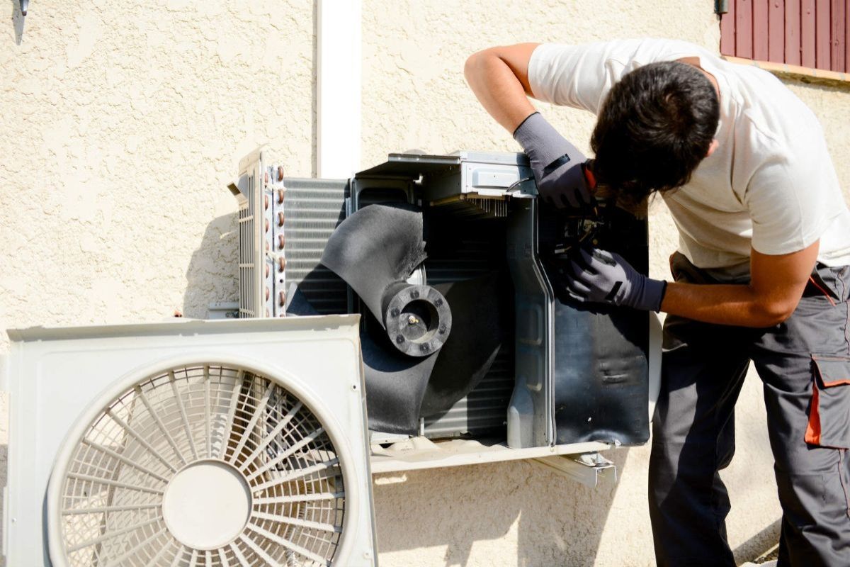 A man is working on a fan on the side of a building.