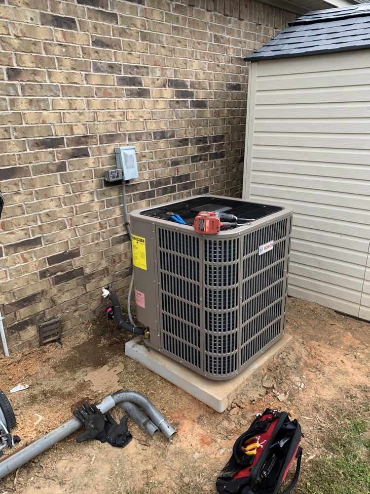 An air conditioner is sitting outside of a brick building next to a shed.