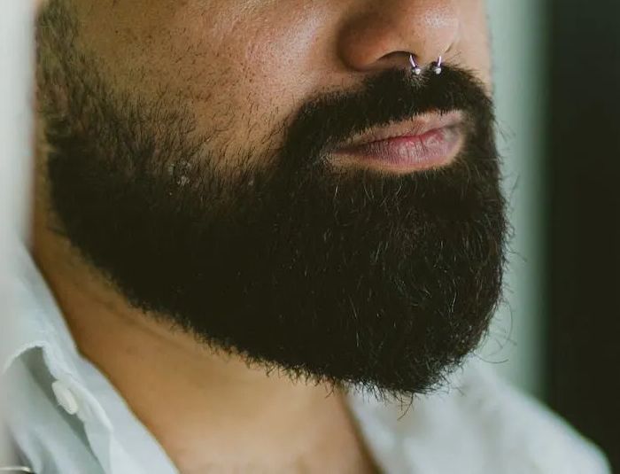 A man with a beard and nose ring is wearing a white shirt.