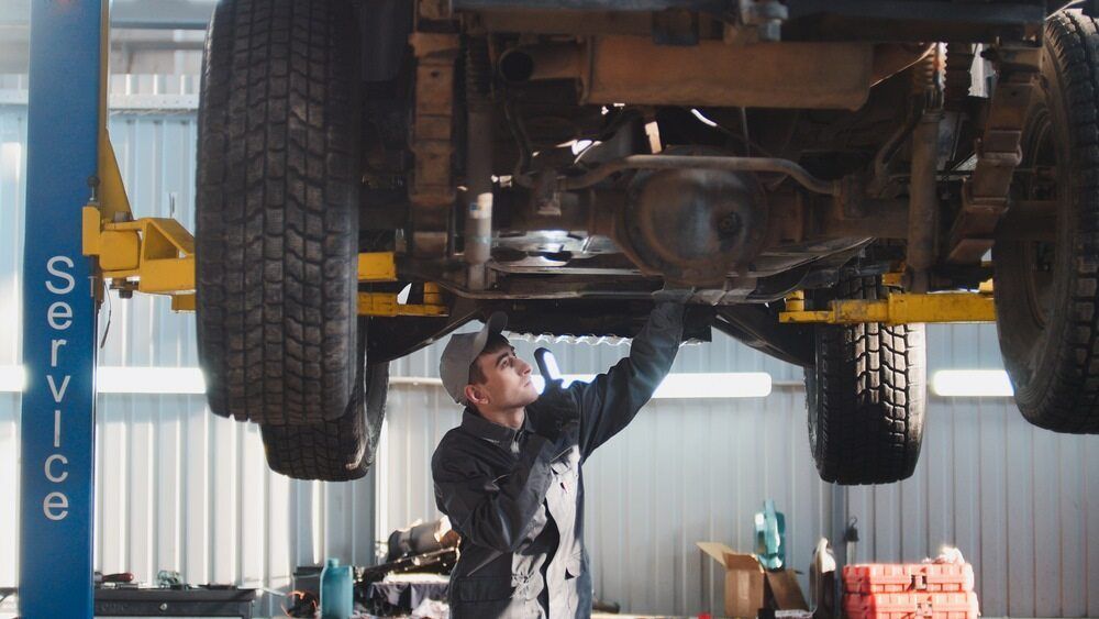 A Man Is Working Under A Car On A Lift In A Garage — Browns Autobahn In Nambour, QLD