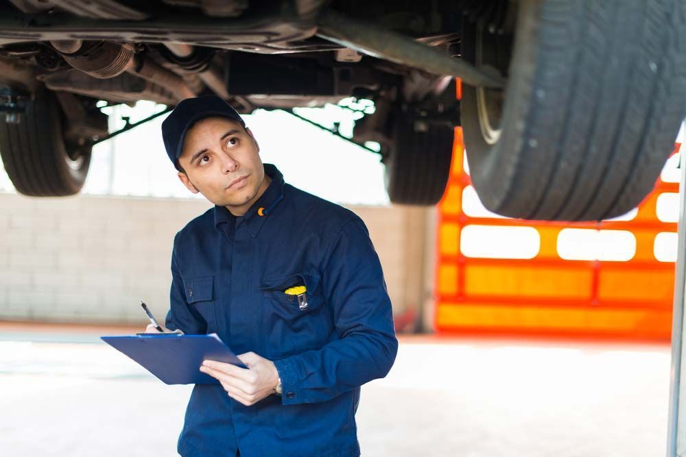 A Mechanic Is Looking Under A Car While Holding A Clipboard — Browns Autobahn In Nambour, QLD