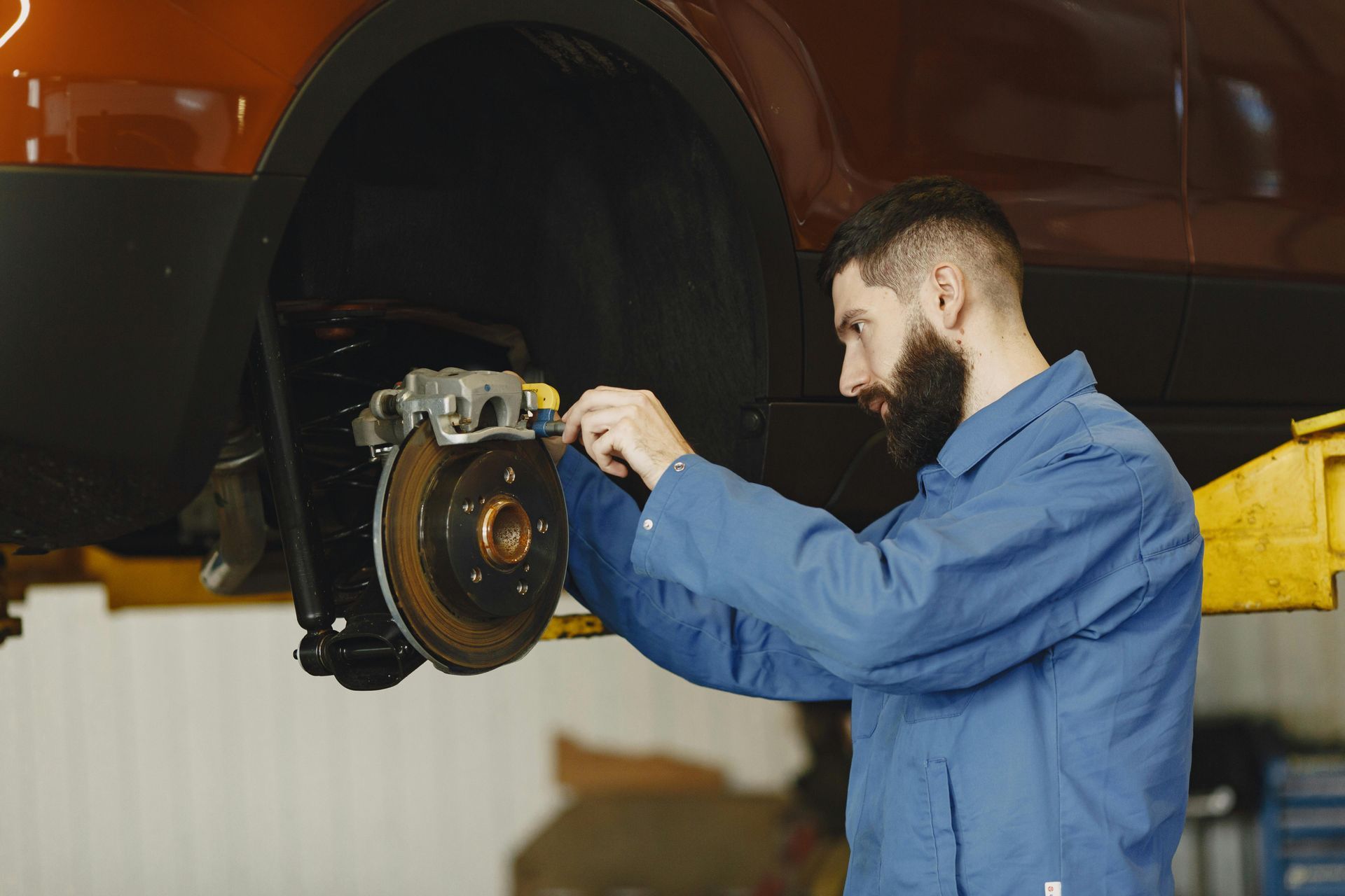 A mechanic in a blue uniform repairs a car brake system in a garage.