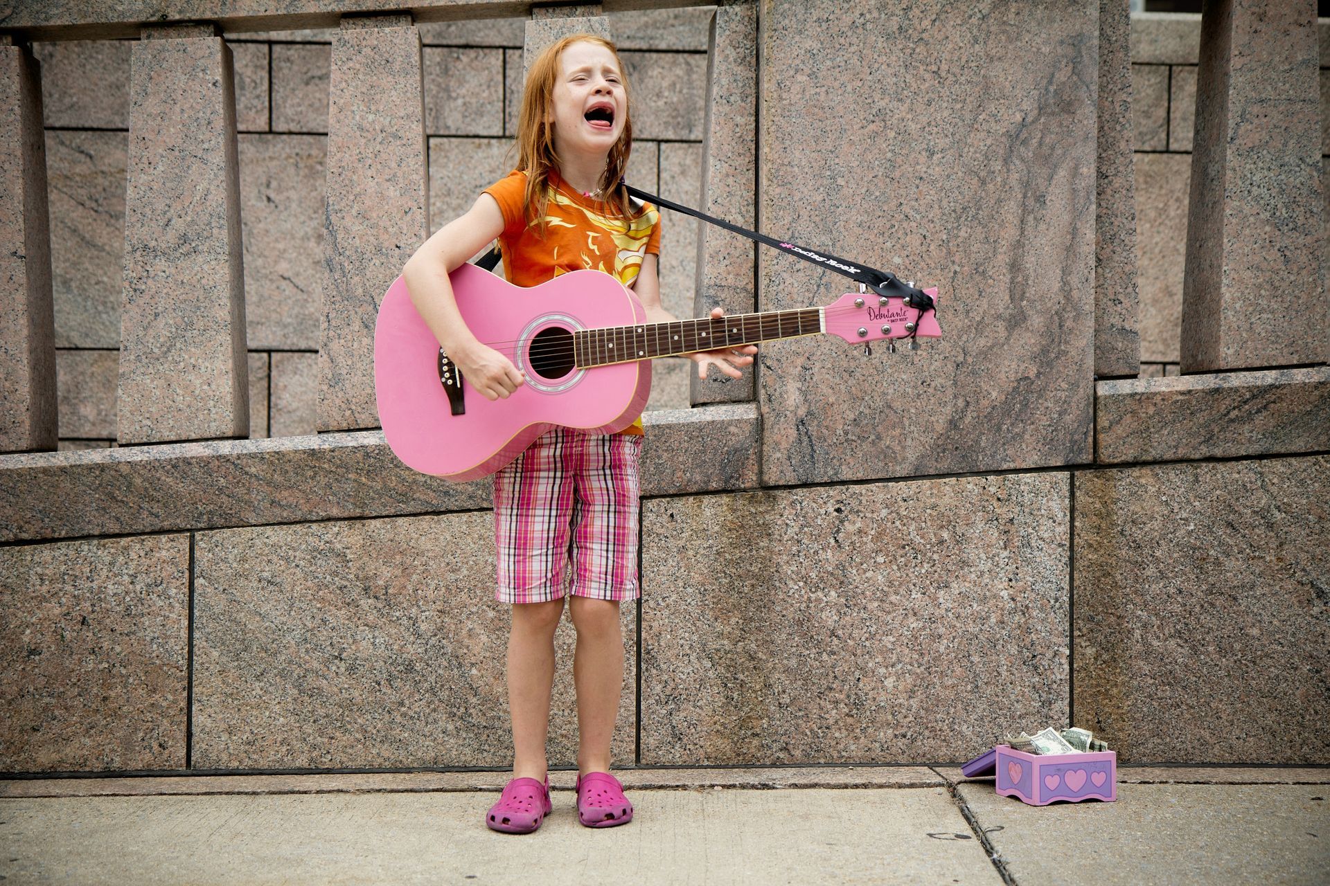 A young girl is singing into a microphone while holding a pink guitar