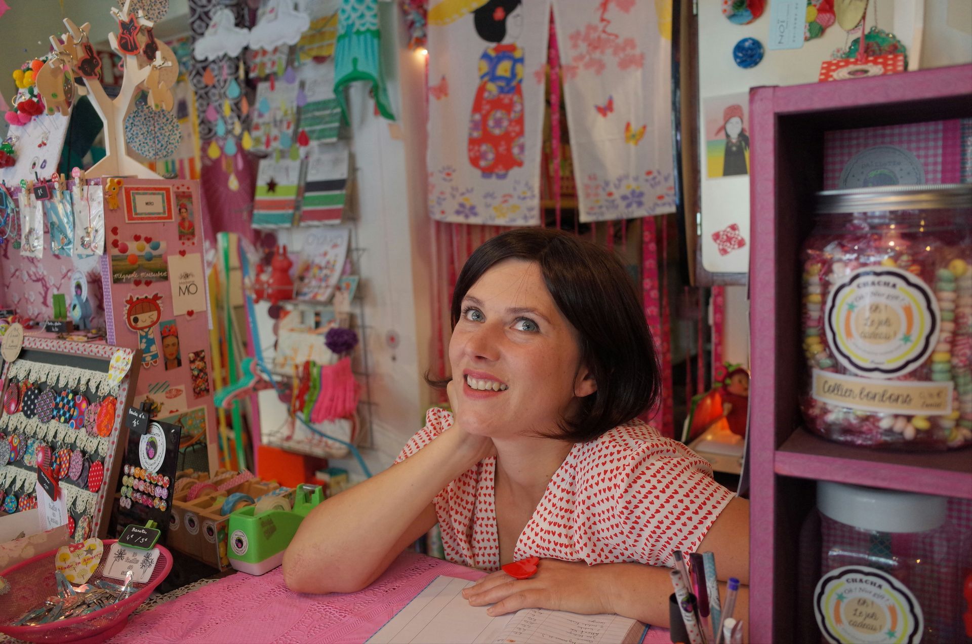 A woman is sitting at a desk in front of a jar of candy