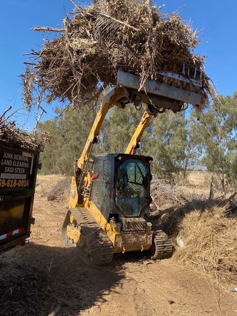 Yellow skid-steer loader lifting a large bale of dry hay on a dirt path