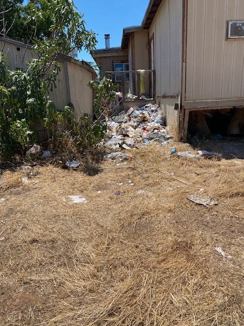 Dry, trash-strewn alley between buildings with a pile of debris and sparse vegetation