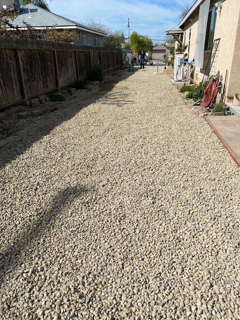 Gravel pathway between houses under a blue sky, with a few people in the distance.