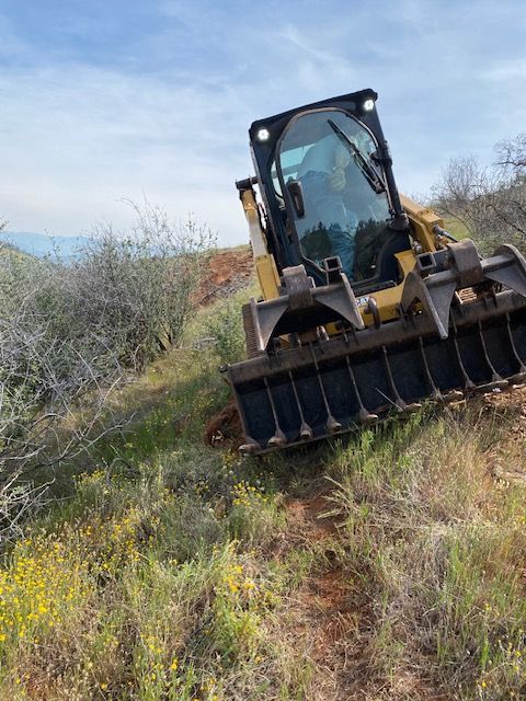 Excavator with front bucket on a grassy hillside under a blue sky