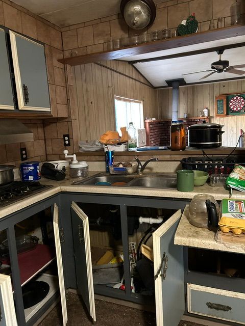 Cluttered kitchen with open cabinets, sink, countertop items, and a ceiling fan above.