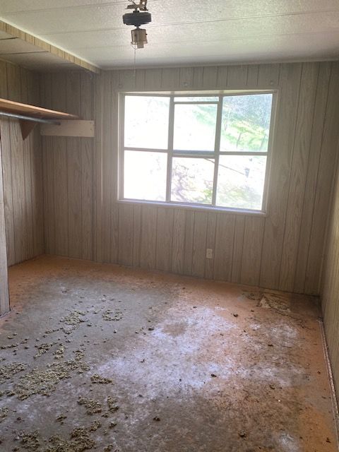 Empty room with wood-paneled walls, a large window, and debris-strewn floor.