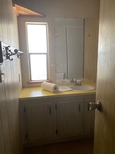 Small bathroom vanity with mirror, yellow countertop, sink, and window with daylight.