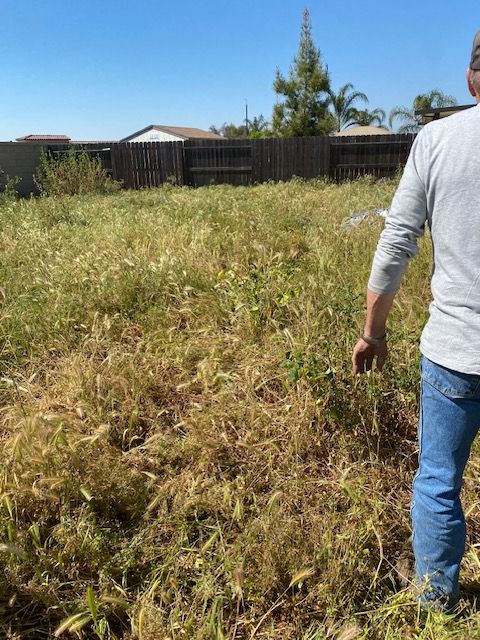 Man standing in a dry grassy field near a fence and houses on a sunny day