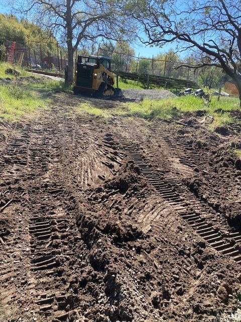 Mud road with deep tire tracks leading to a bulldozer in a grassy wooded area.