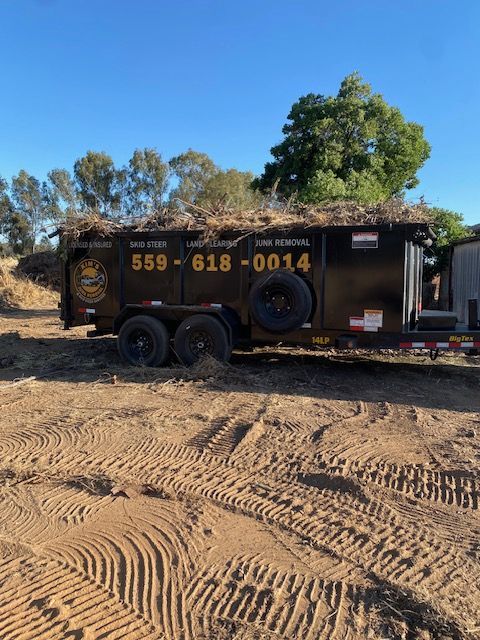 Black dumpster trailer with phone number, parked on dirt under a blue sky.