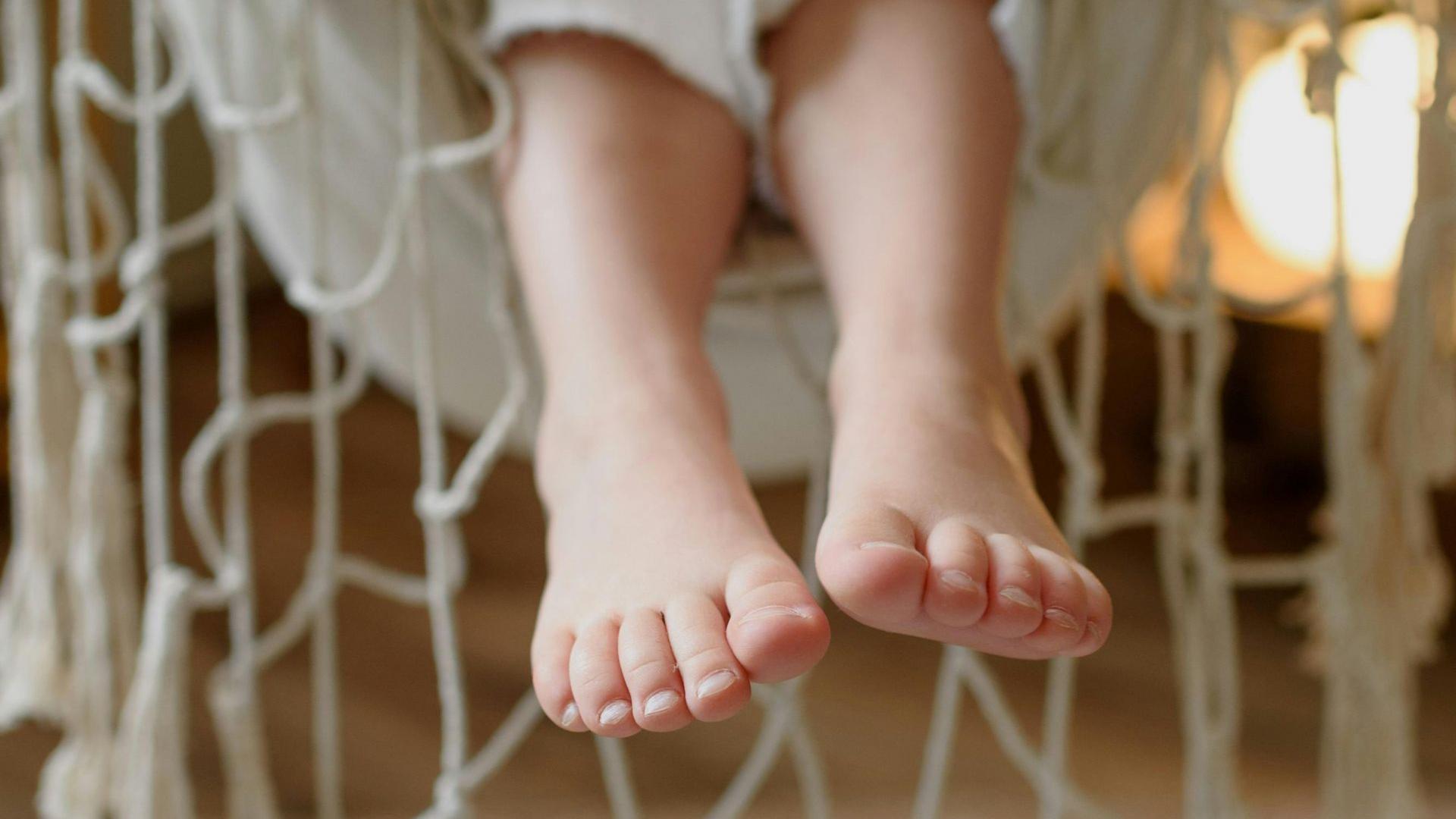 Blote voeten rustend in een macramé hangmat. Crèmewit net, zachte verlichting.
