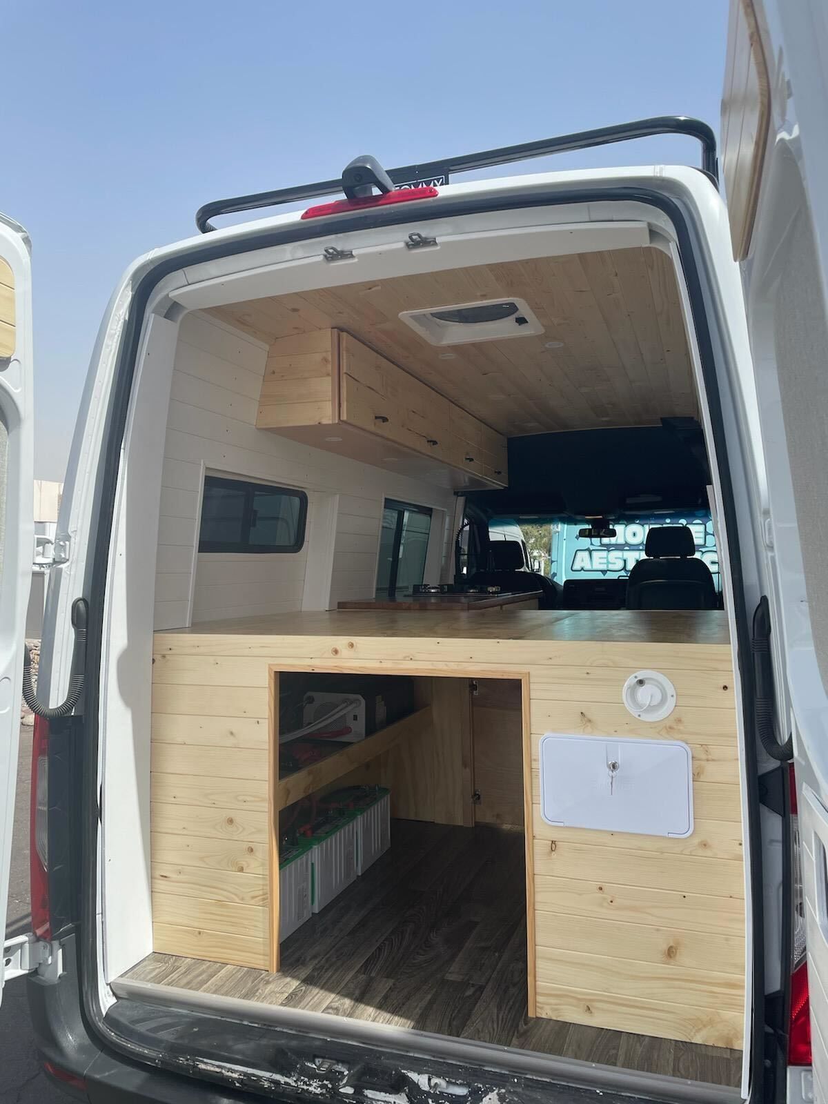 The back of a white van with wooden cabinets and a bed.