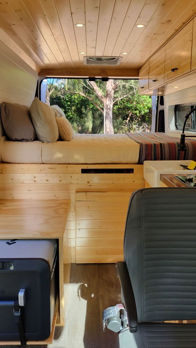 The inside of a camper van with a bed and luggage.