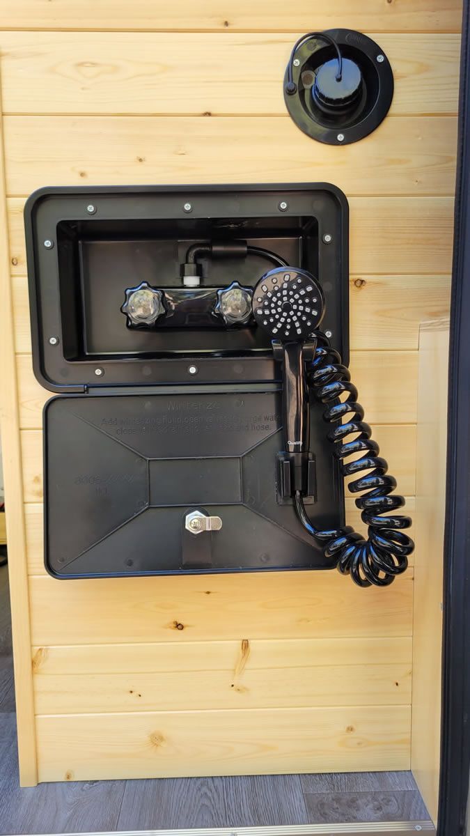 A shower head is hanging from the side of a wooden wall.