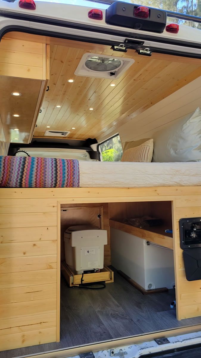 The inside of a van with a bed and a refrigerator.