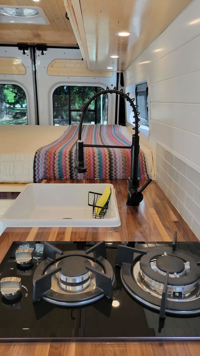 A kitchen in a van with a stove top oven and a sink.