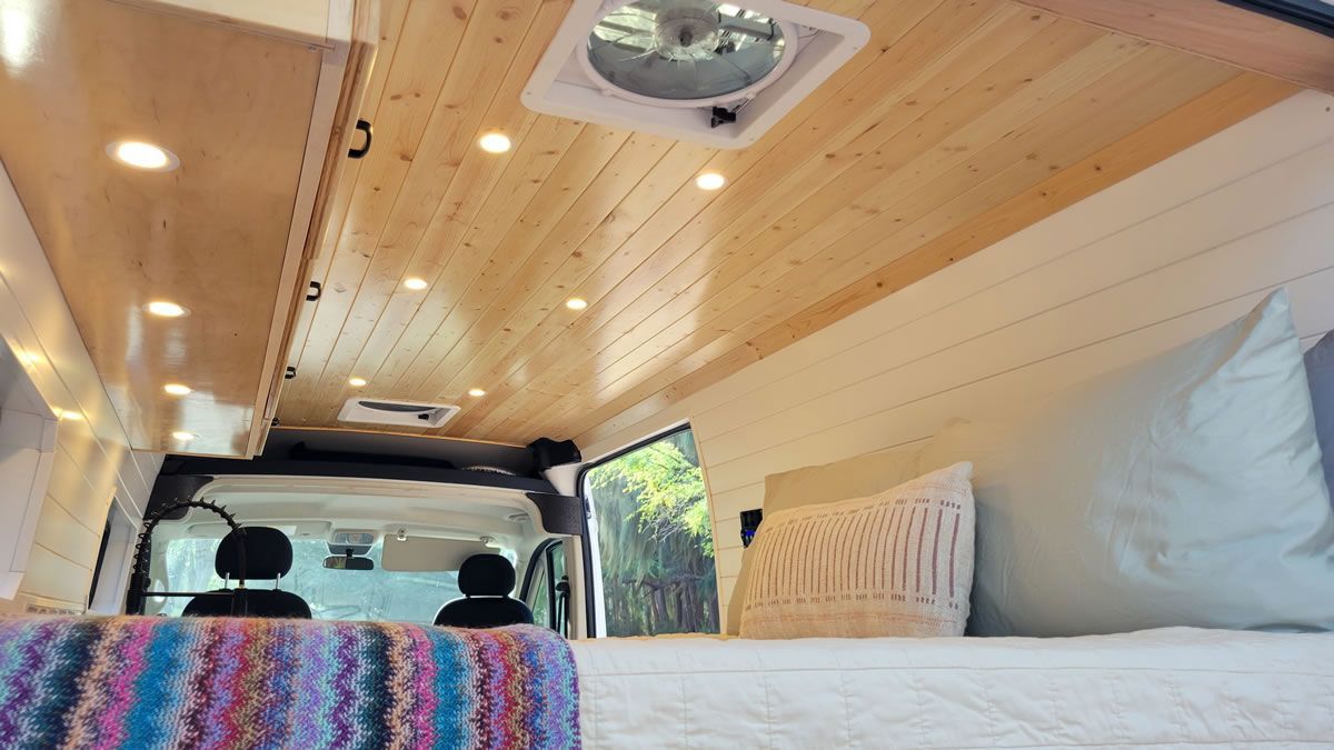 The inside of a van with a bed and a fan on the ceiling.