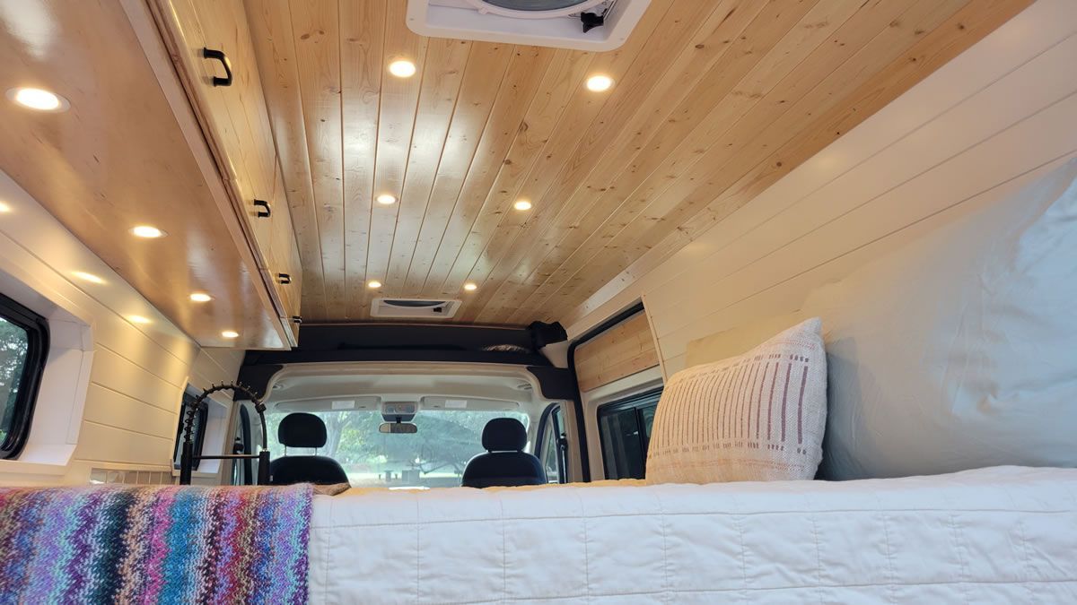 The inside of a van with a wooden ceiling and a bed.