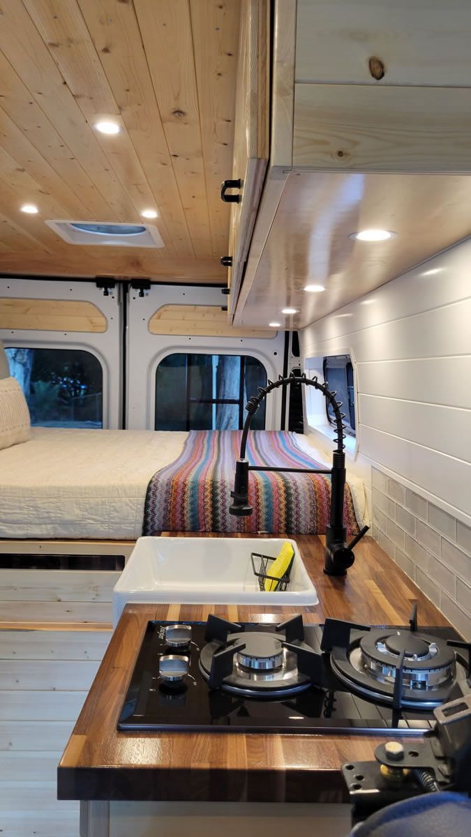 A kitchen in a van with a sink , stove , and bed.