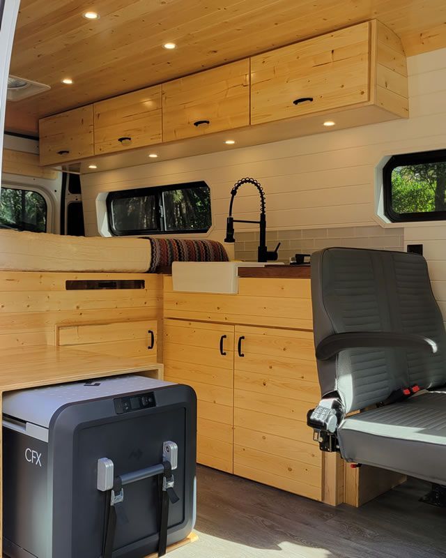 The inside of a camper van with wooden cabinets and a refrigerator.