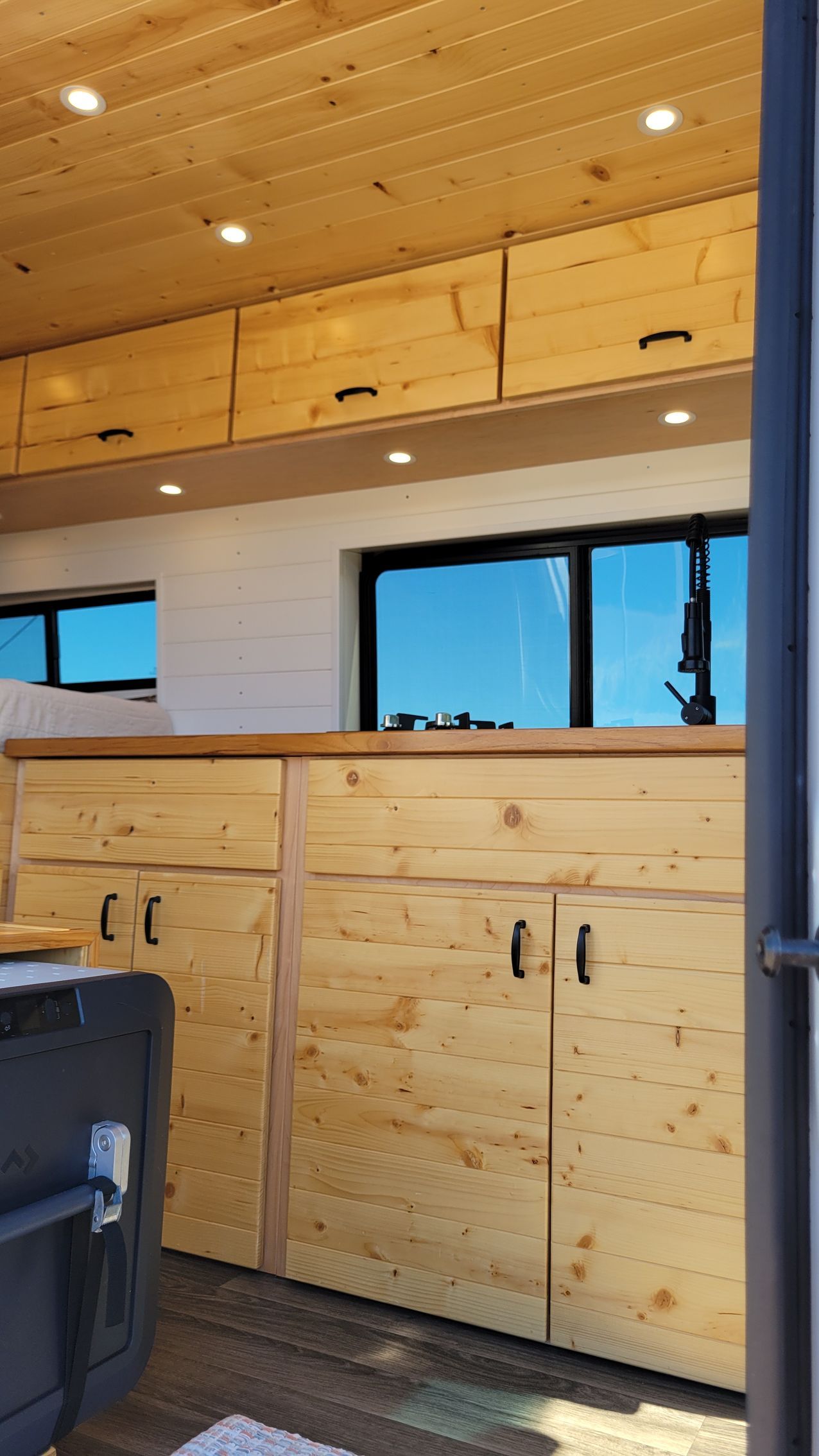 A kitchen in a van with wooden cabinets and a window.