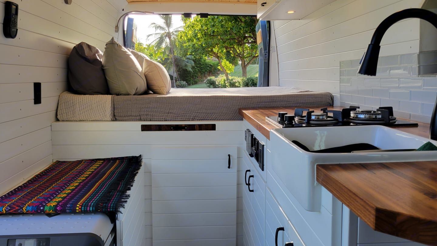 A kitchen in a van with a sink , stove , and bed.