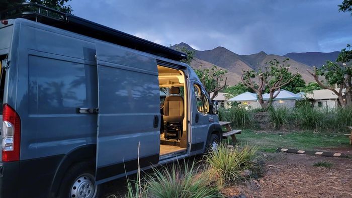 A camper van is parked in a field with its doors open.