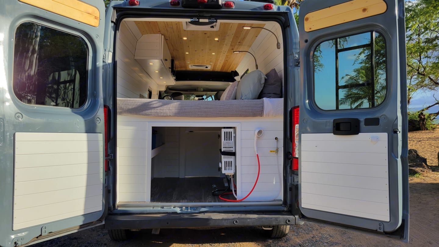 The back of a van with its doors open and a bed in it.