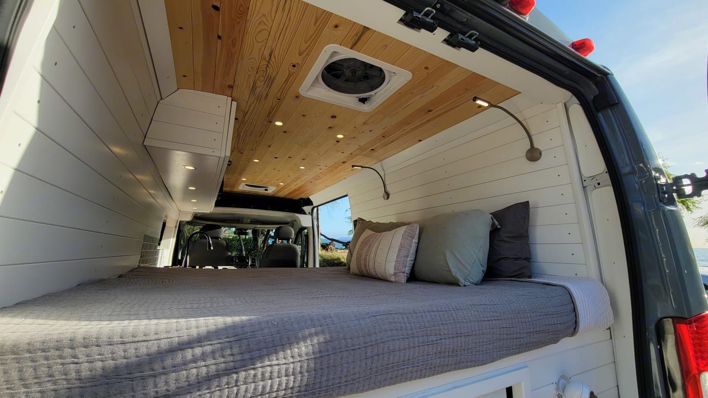 The inside of a van with a bed and a fan on the ceiling.