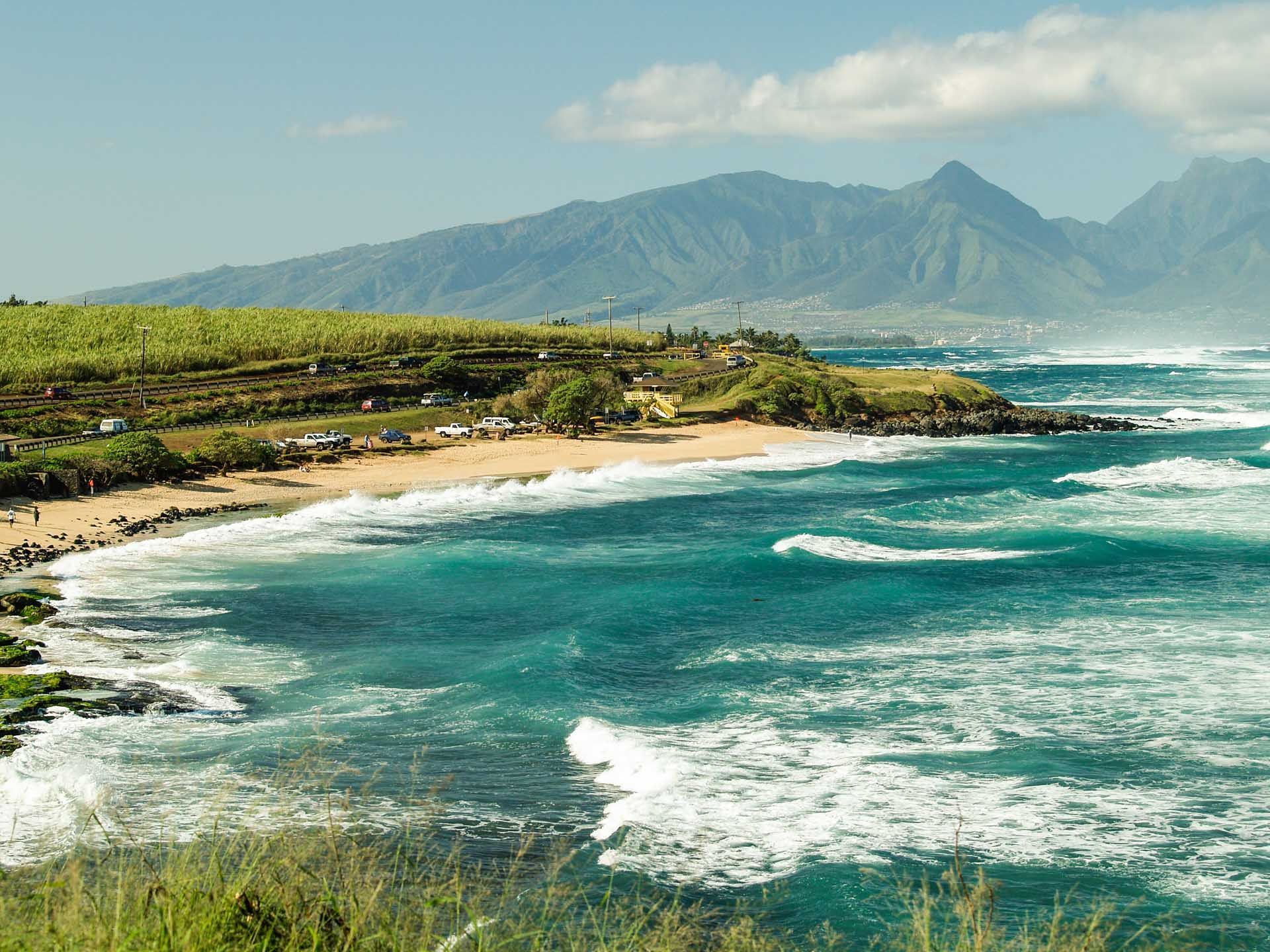 A beach with mountains in the background and waves crashing on the shore
