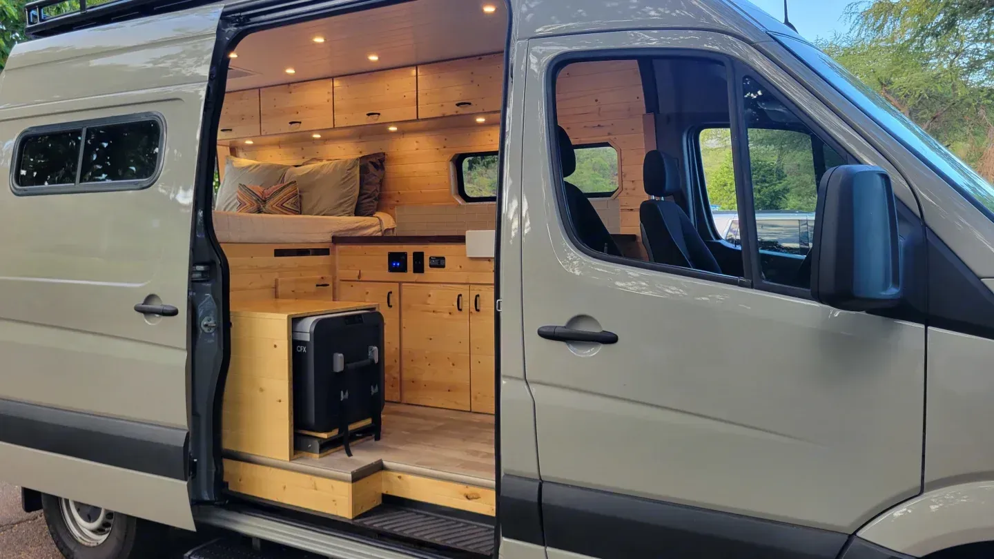 Camper van showing kitchen through side entry with wood finish available for rental by Mana Vans in Wailea, Maui, HI.