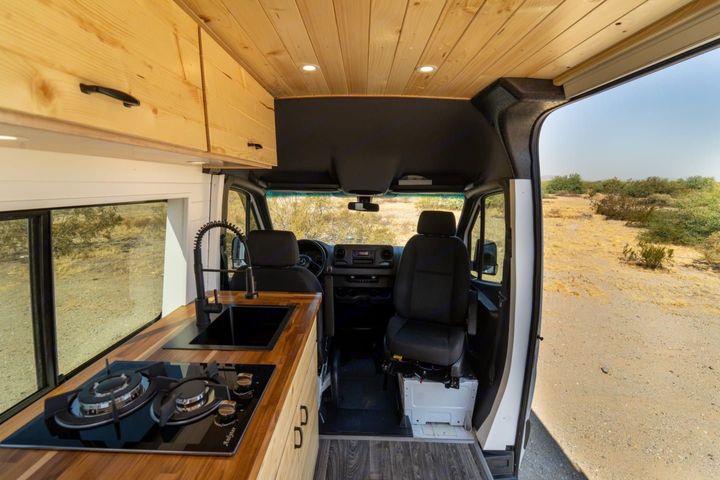 The inside of a van with a kitchen and stove top oven.