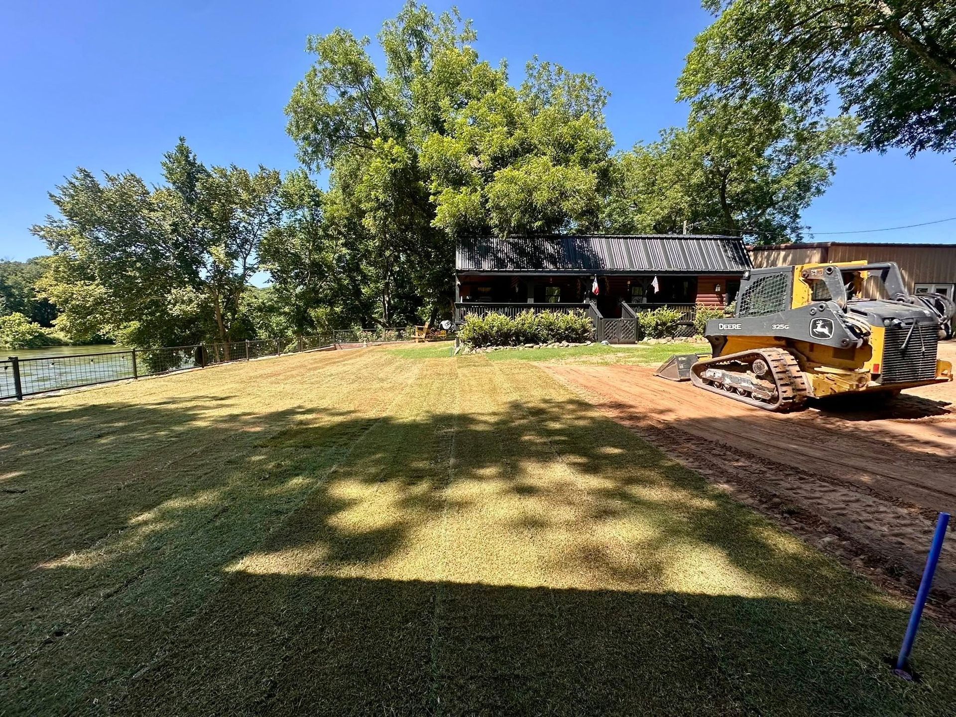 Woman in straw hat smiles, holding wine glass near a lake.