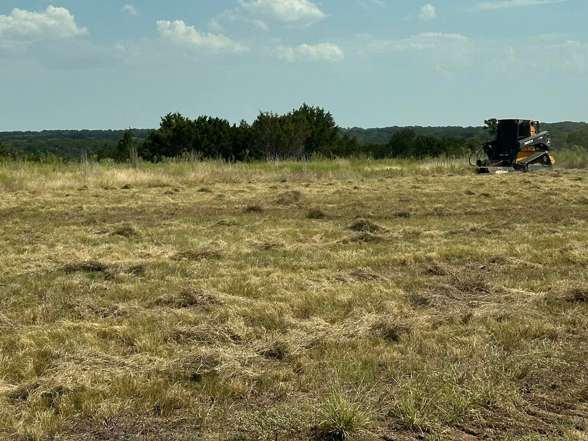 Woman in straw hat smiles, holding wine glass near a lake.