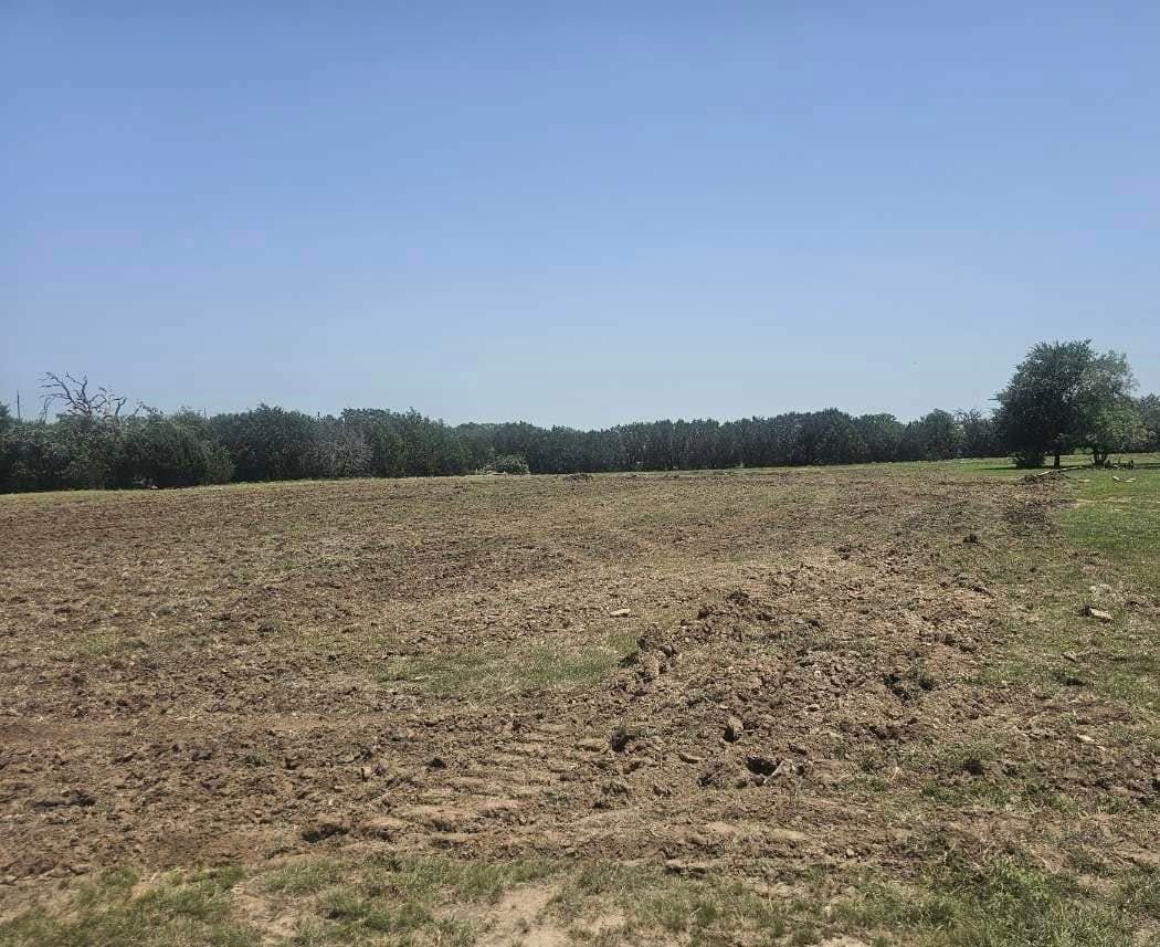 Woman in straw hat smiles, holding wine glass near a lake.