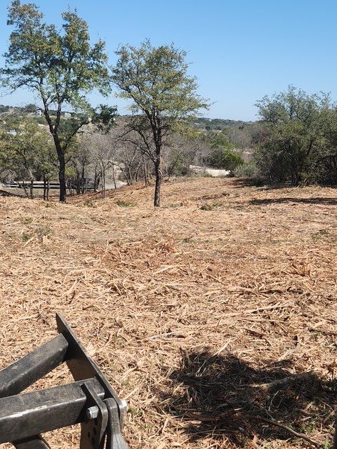 Woman in straw hat smiles, holding wine glass near a lake.