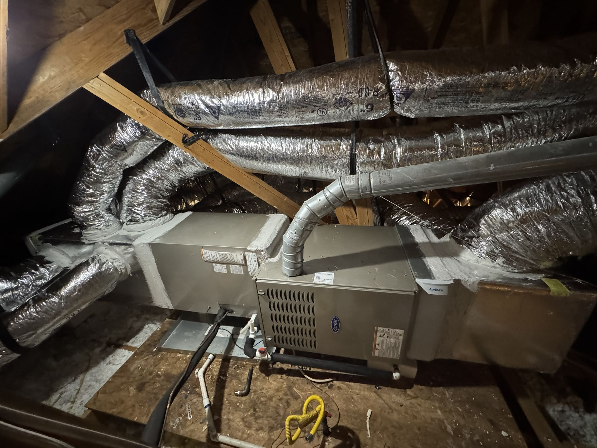 HVAC unit in an attic with ductwork, wooden beams, and insulation.