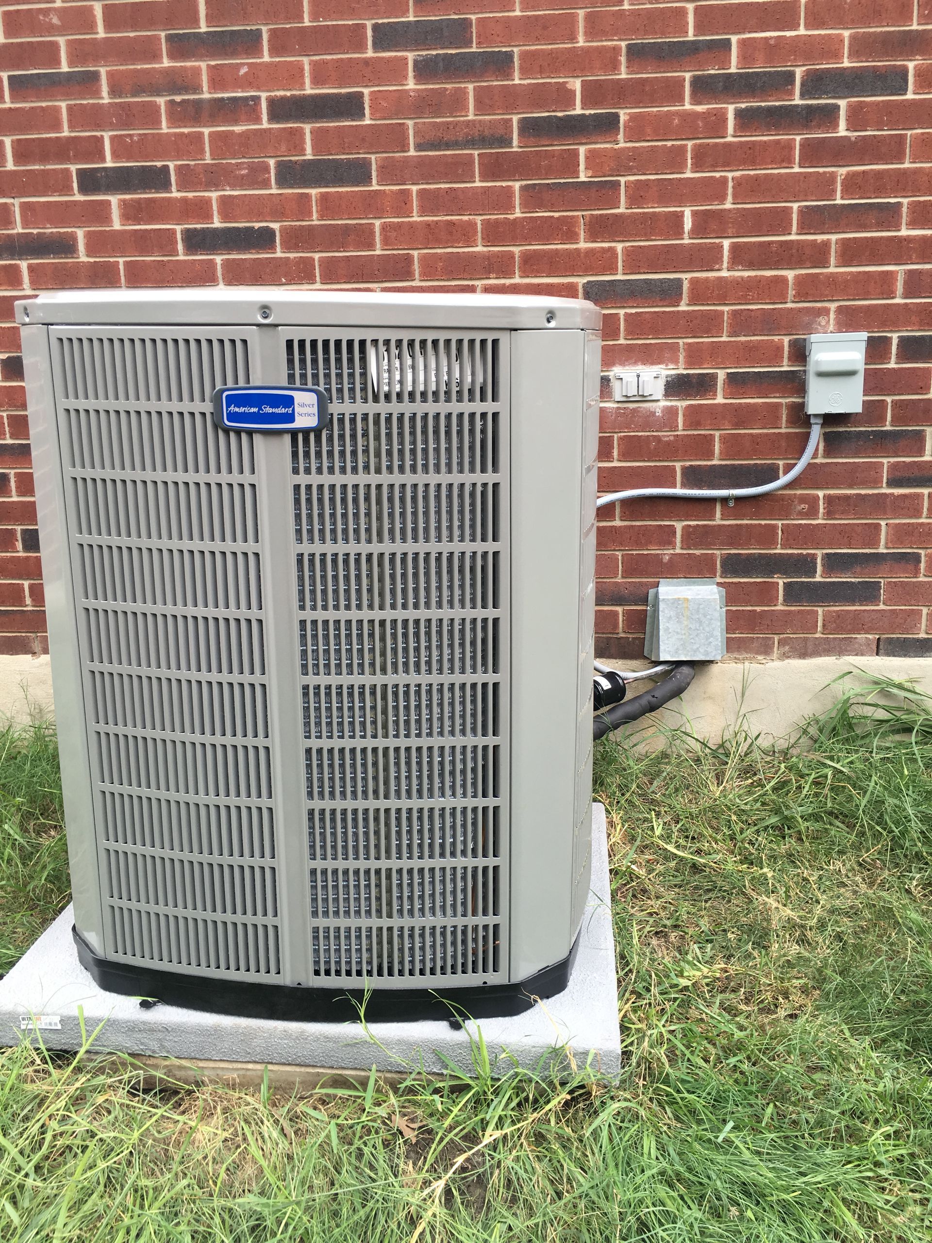 An American Standard air conditioning unit outside a brick building.